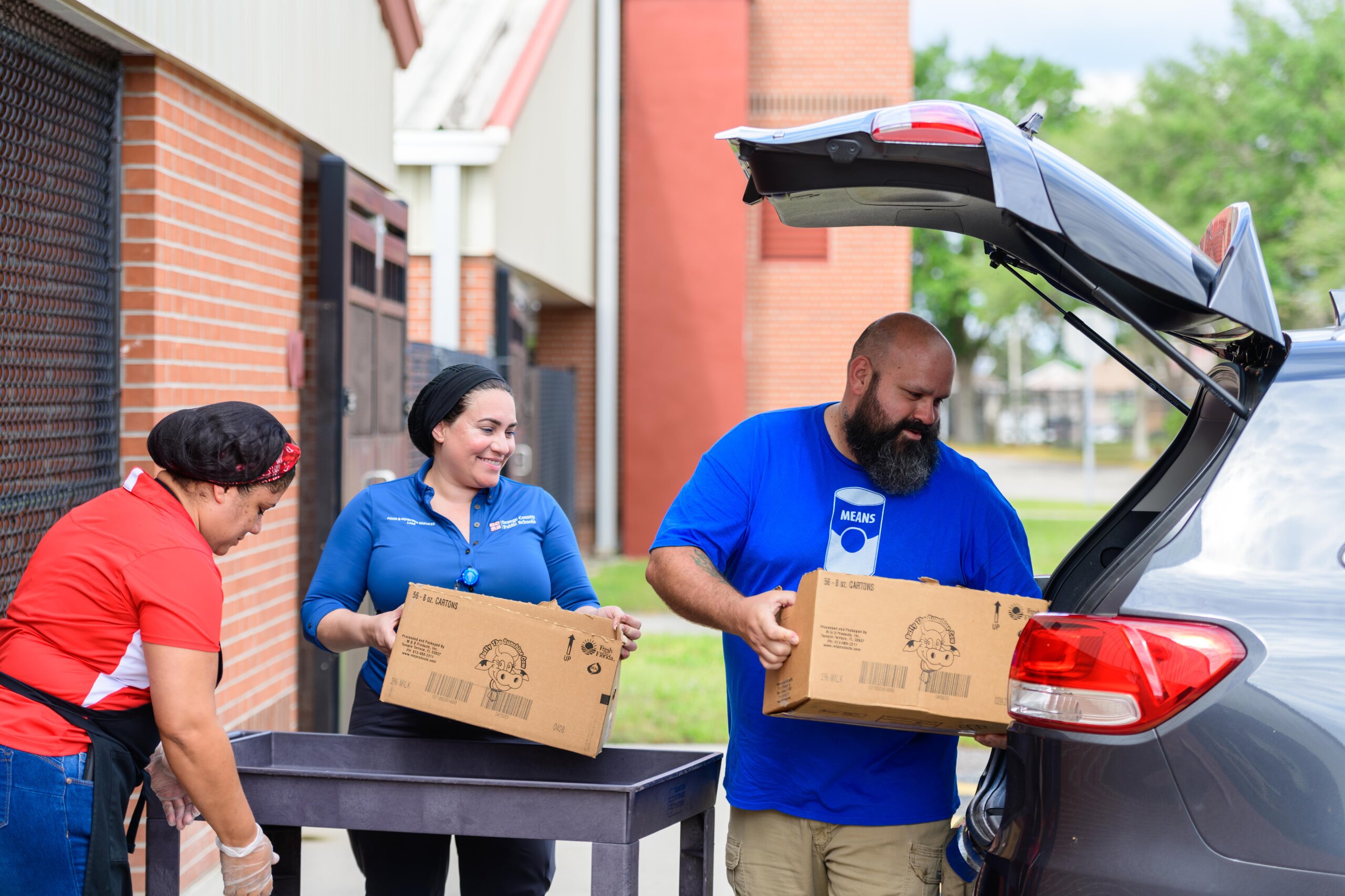 Three people unloading a car with boxes of donated food.